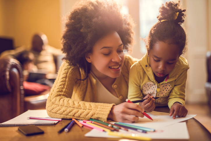 Happy African American mother assisting her daughter in coloring.
