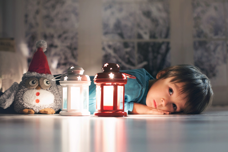 Beautiful little boy, lying down on floor, looking at candle